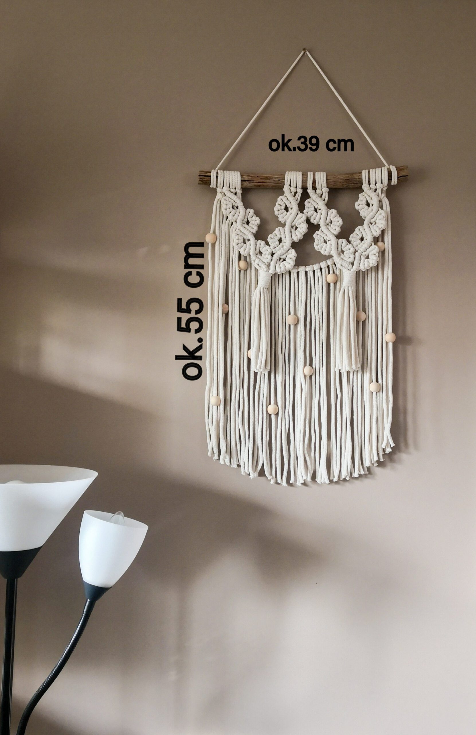 Unikalna makrama ścienna wykonana z ekologicznego sznurka bawełnianego w kolorze ecru o szerokości ok 39 cm i długości ok 55 cm. Charakterystyczny wzór z ozdobnymi splotami i licznymi drewnianymi koralikami. Zawieszona na naturalnej gałęzi, idealna do wnętrz w stylu skandynawskim, boho lub rustykalnym.
