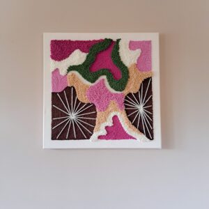 Kwadratowy obraz teksturowany techniką punch needle, 50x50 cm, wykonany z bawełny, akrylu i wełny. Przedstawia abstrakcyjne kształty i promienie, dominują odcienie różu, zieleni, brązu i kremu.